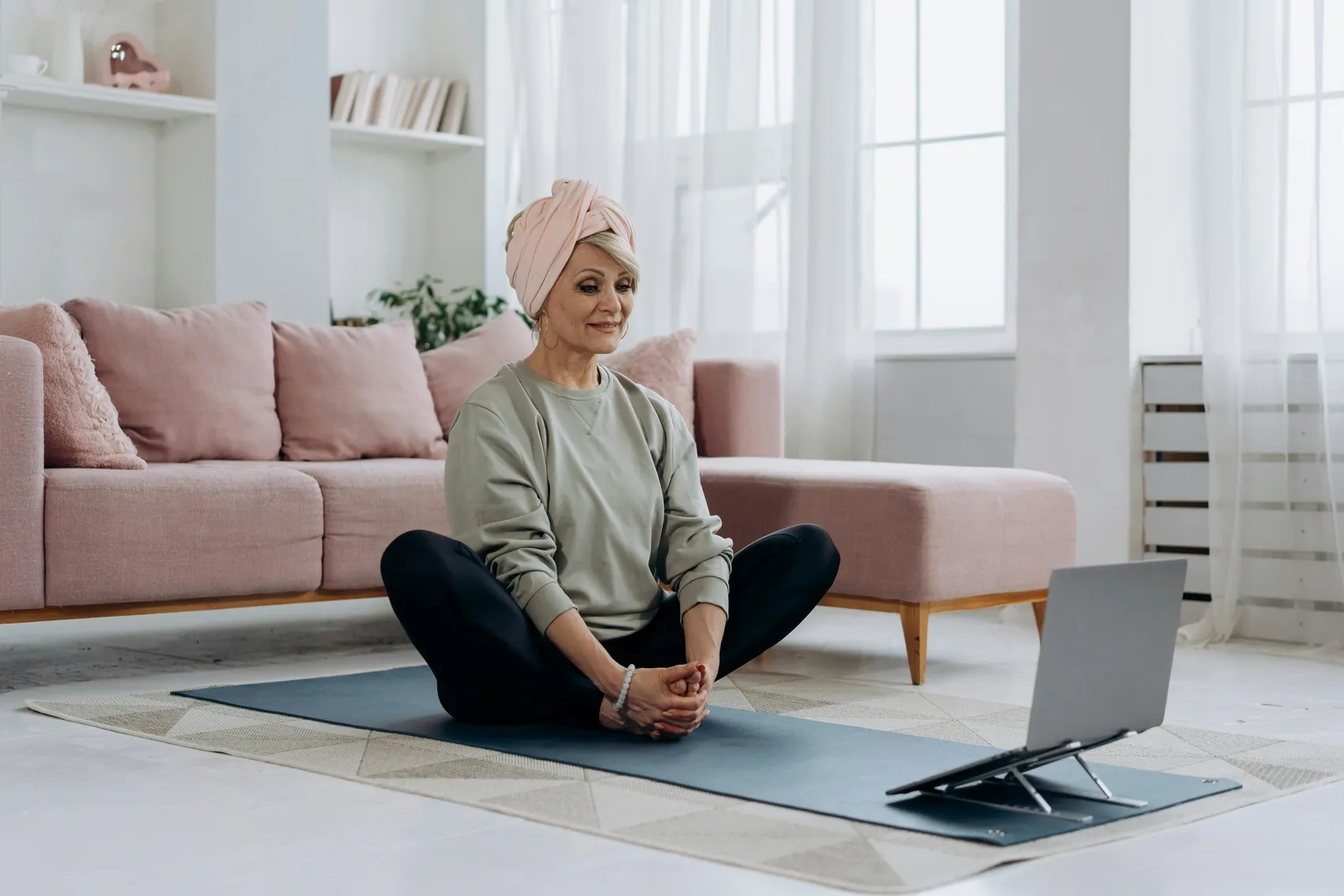 A person following a guided session on a laptop while sitting on a yoga mat